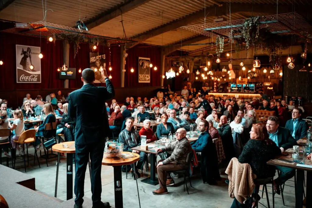 A speaker addressing a large crowd in a vibrant, warmly-lit indoor venue.