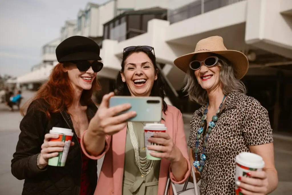 Three happy women taking a selfie outdoors while enjoying coffee together.