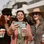 Three happy women taking a selfie outdoors while enjoying coffee together.