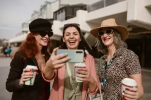 Three happy women taking a selfie outdoors while enjoying coffee together.