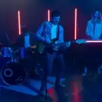 A dynamic live band performing with vibrant neon lights, featuring drums, guitar, and keyboard.