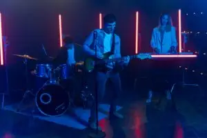 A dynamic live band performing with vibrant neon lights, featuring drums, guitar, and keyboard.